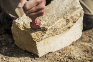 Construction worker holding a chisel, working on a stone.